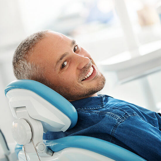 A man lying in a dental chair while showing his white teeth