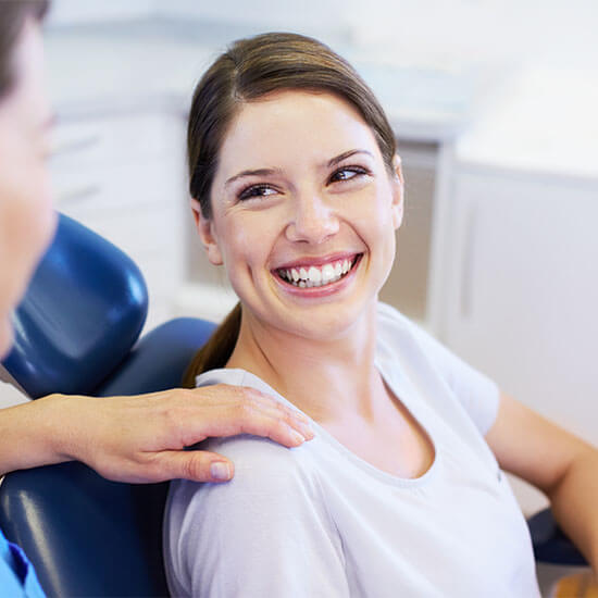 A young woman sitting in a dental chair while showing her white smile 